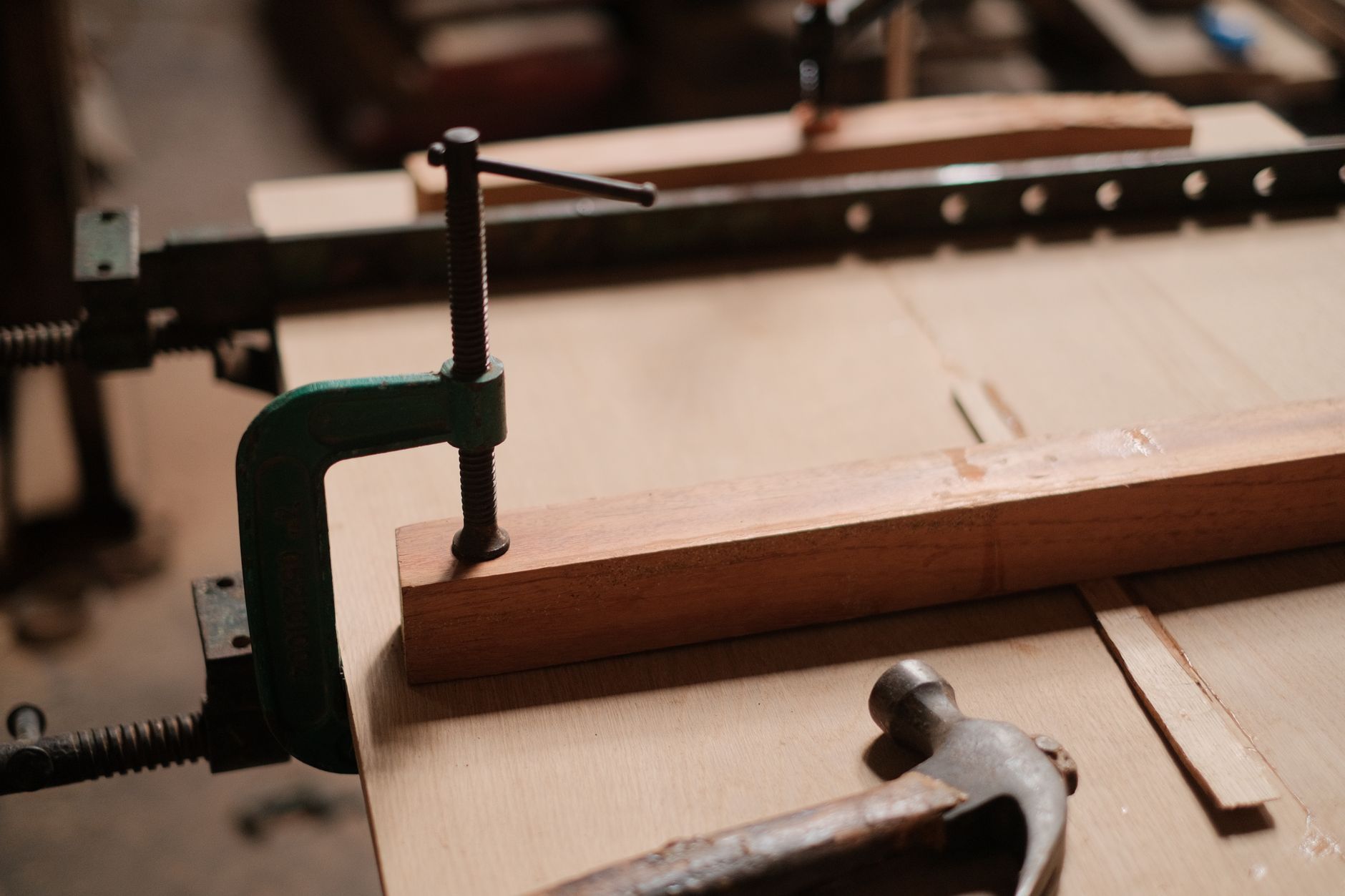 Detailed view of clamps holding wood in place alongside a hammer in a workshop.