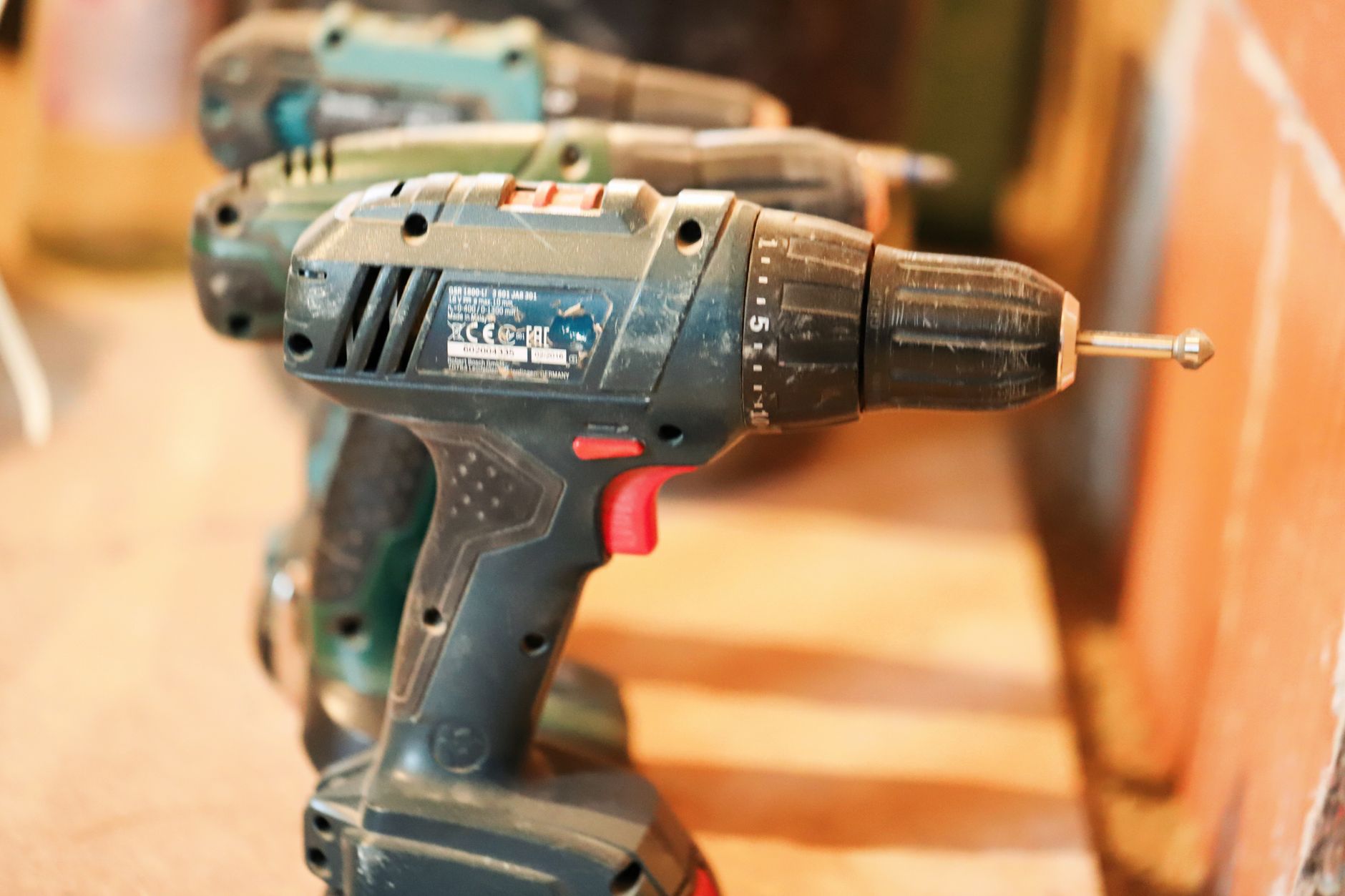 A selection of cordless drills with visible features such as clutches, chucks, and battery packs, arranged on a workbench.