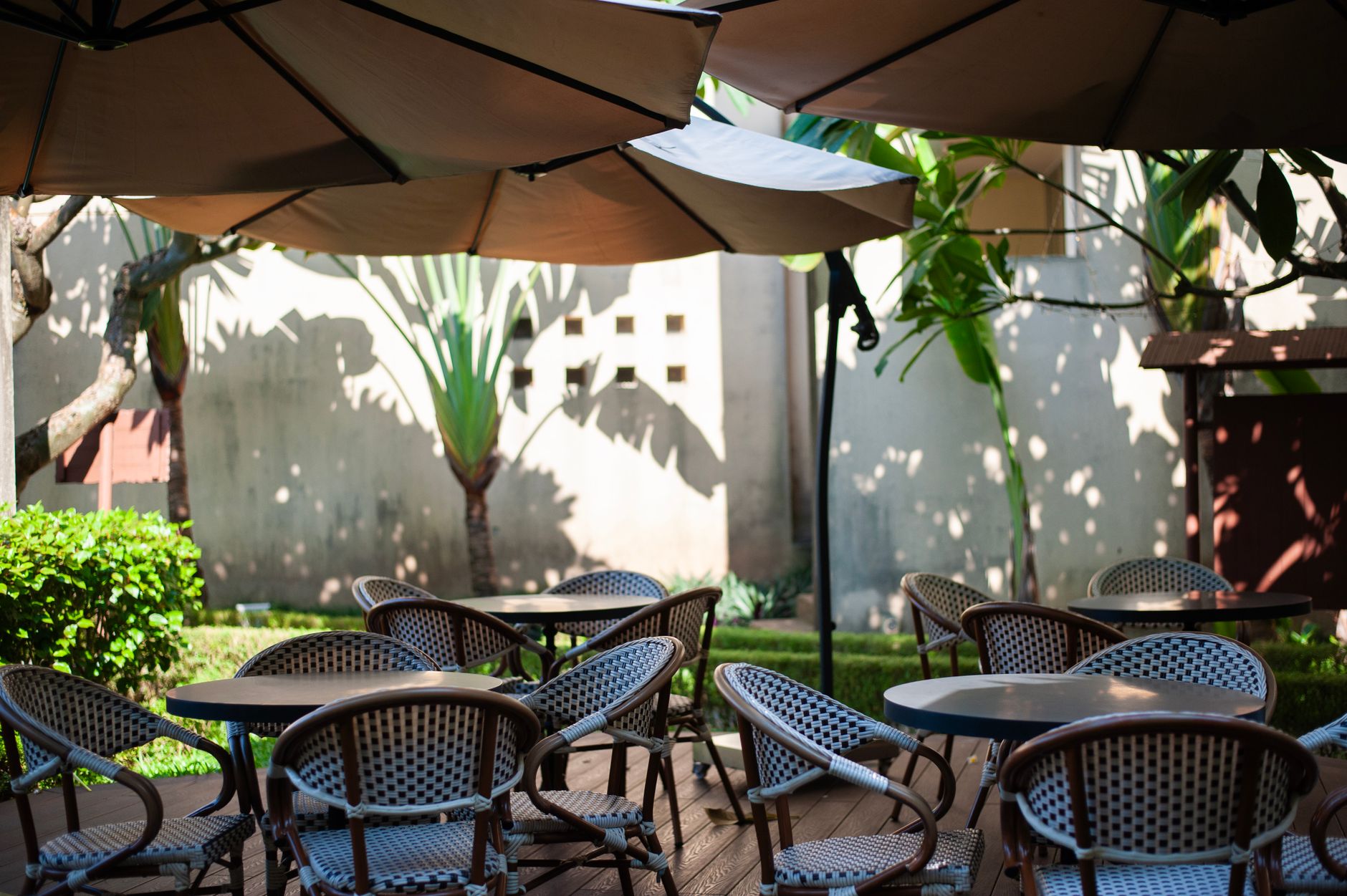 Sunlit outdoor café terrace featuring empty tables, chairs, and large umbrellas.