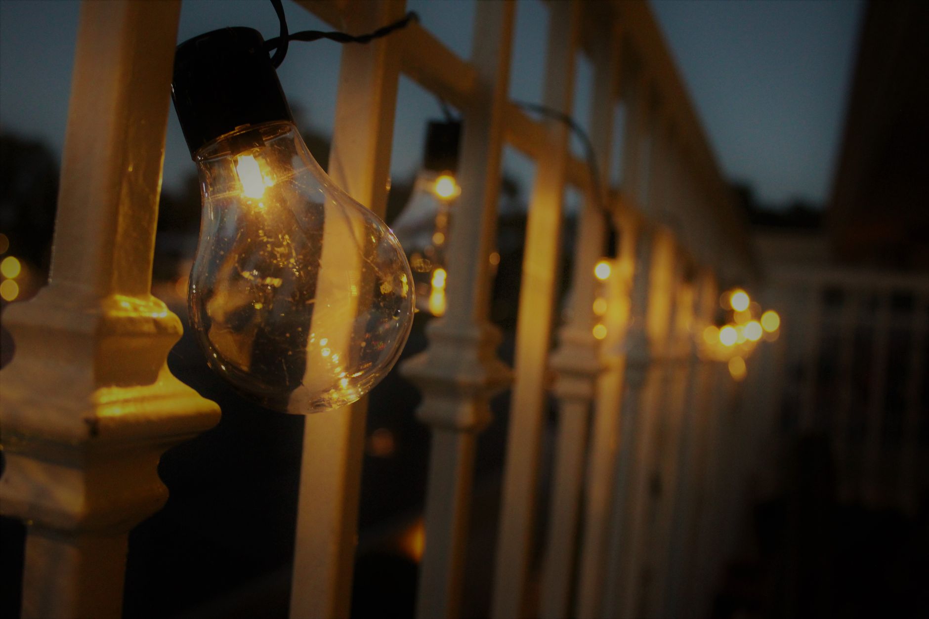 Warm glow from string lights hanging on a railing during evening twilight.